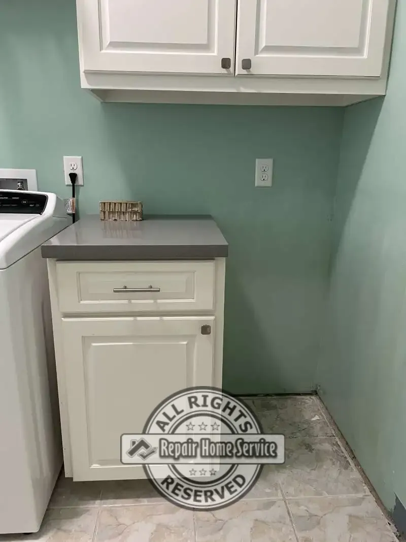 Completed laundry room cabinet renovation featuring custom drawer, white raised-panel cabinetry, gray countertop, and dedicated freezer space.