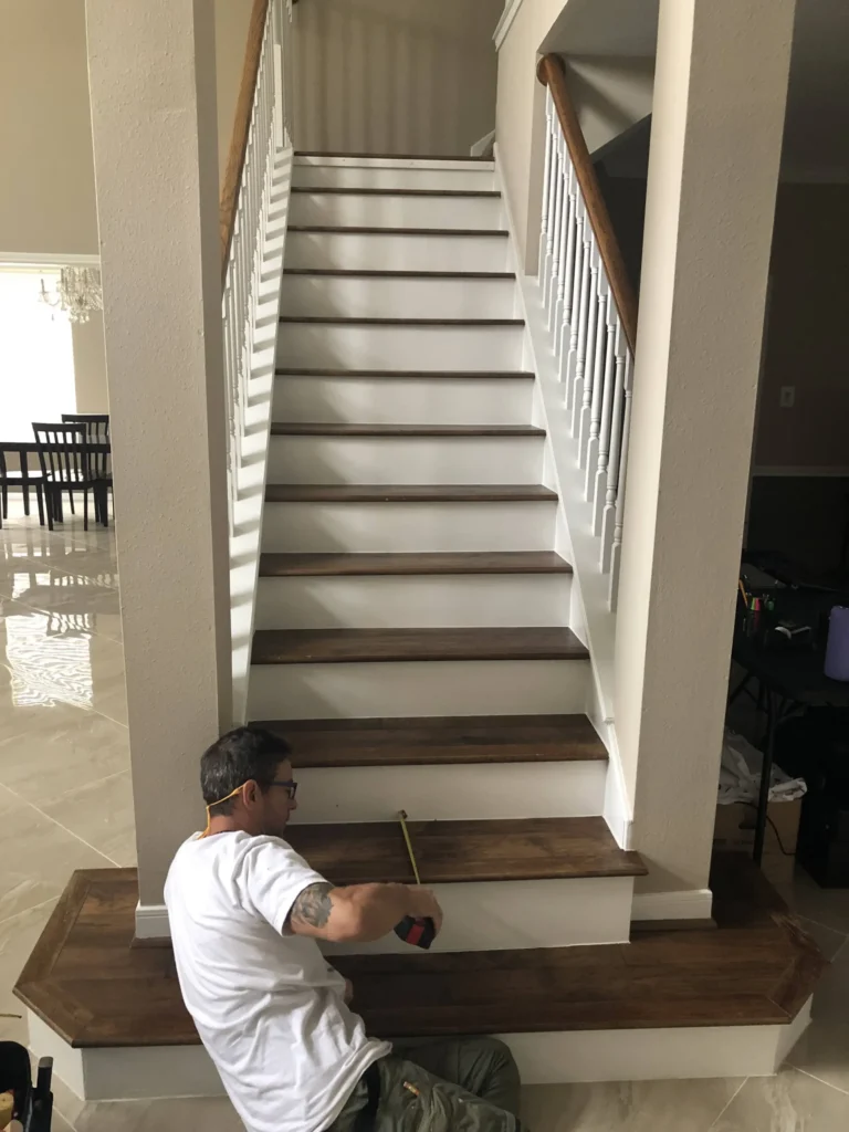 Carpenter measuring a newly installed dark Red Oak stair tread during a custom stair remodel in a Cypress TX home with white risers and polished tile flooring.