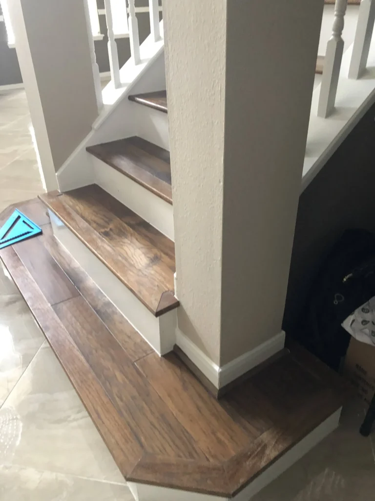 Detail of custom mitered Red Oak starter tread stained Black Coffee with white maple risers wrapping a beige column during a Cypress TX stair rebuild.