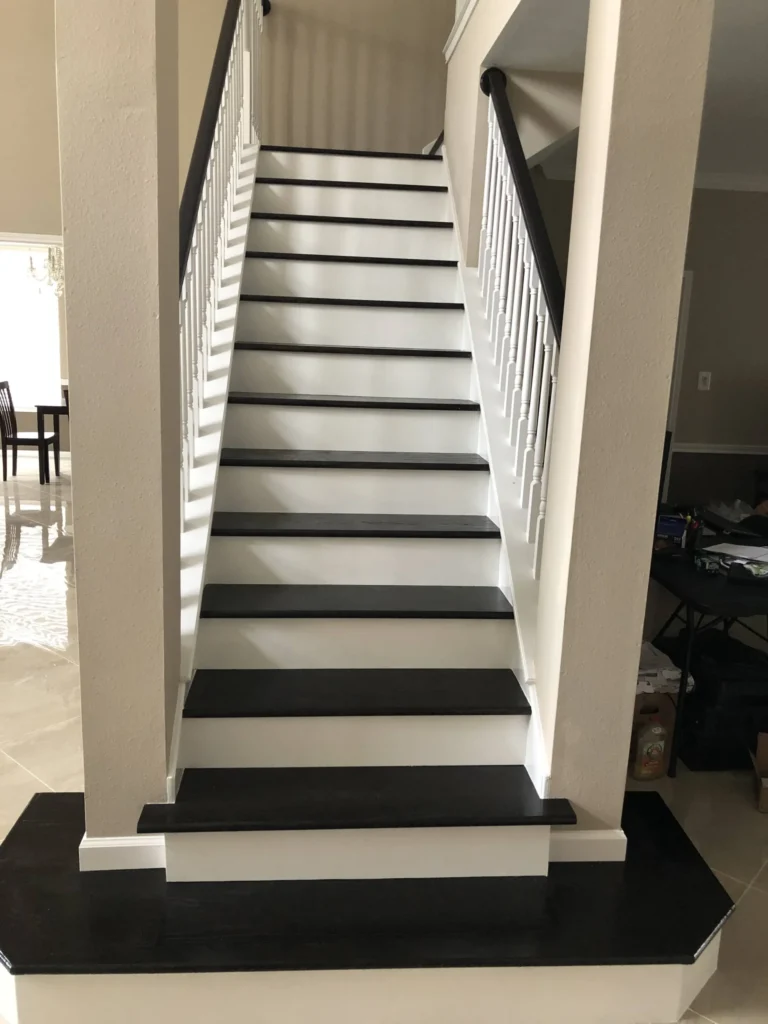 Full straight-run staircase after remodel in Cypress TX with Black Coffee stained Red Oak treads, white maple risers, glossy handrail, and white spindles between beige walls.