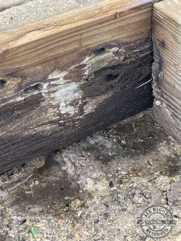 Severely rotted deck rim joist corner with crumbling wood and damp soil underneath a Houston TX lakeside deck before repai
