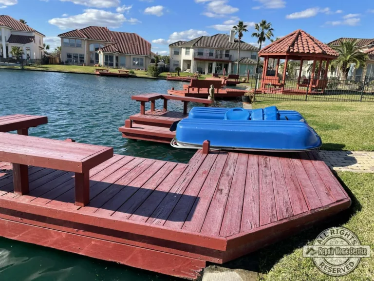 Finished Houston TX deck and dock with four-coat red stain, built-in seating, paddle boat, and suburban homes across the lake.