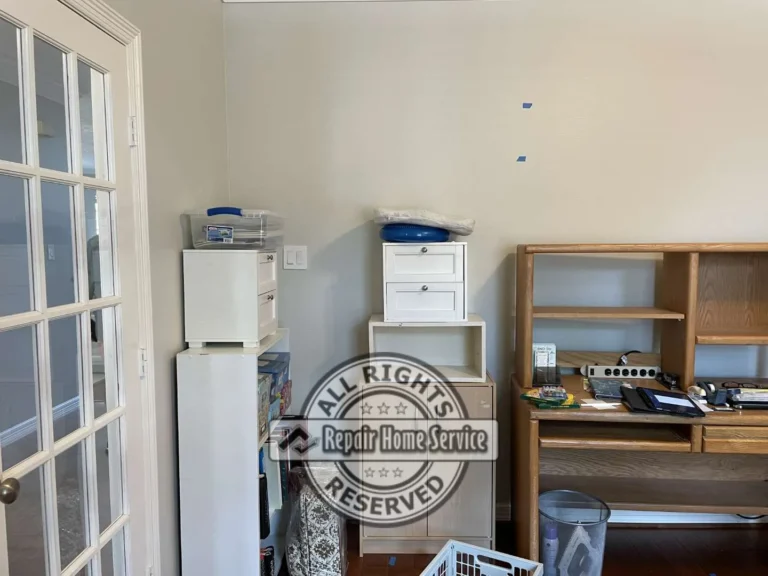 Before condition of craft room corner in Cypress TX showing oak desk with hutch, stacked white storage drawers, French door entry, and blue tape marking planned custom cabinet installation.