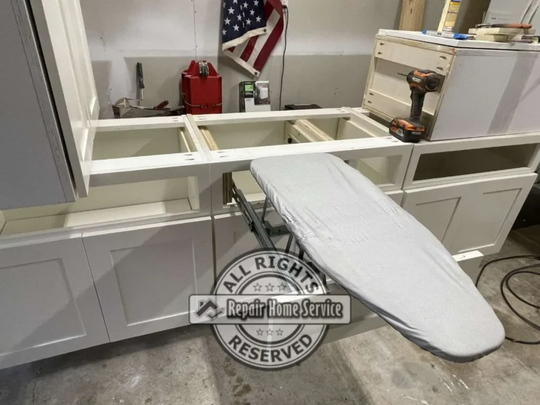 Shop-built white shaker base cabinets in Houston area workshop with custom pull-out ironing board extended on metal drawer slides before granite countertop installation.
