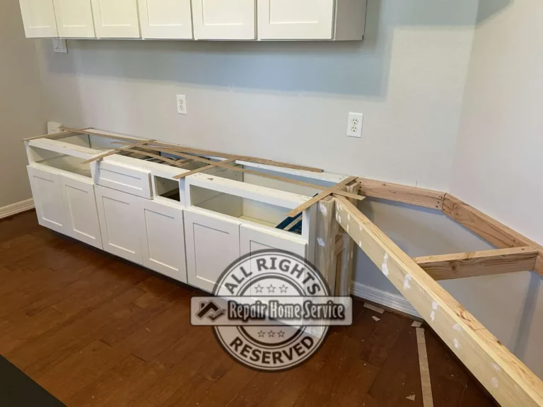In-progress craft room cabinet installation in Cypress TX with white base and wall cabinets set on dark wood floors and raw wood desk framing built into the corner.