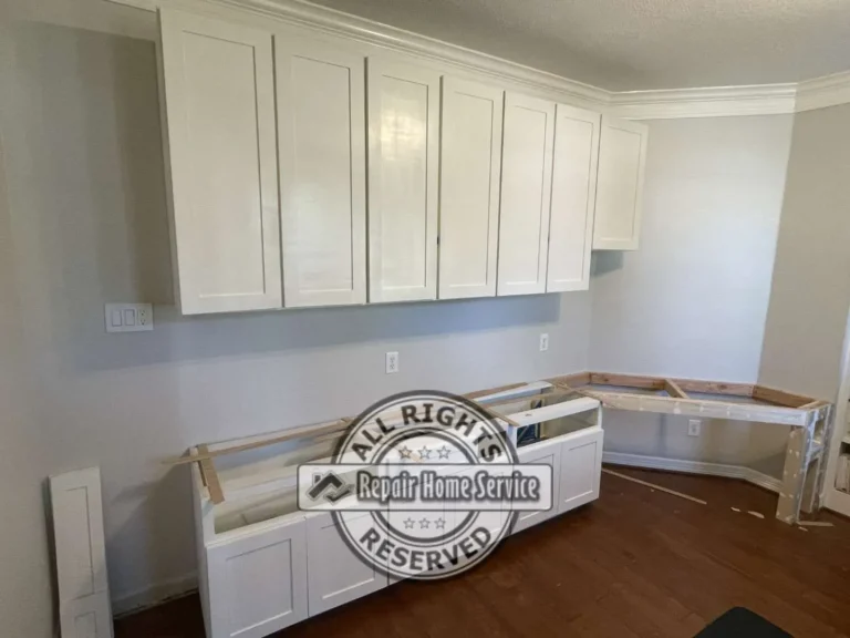 Upper shaker wall cabinets mounted to ceiling and crown molding during craft room remodel in Houston area home with desk framing and electrical outlets at backsplash height.