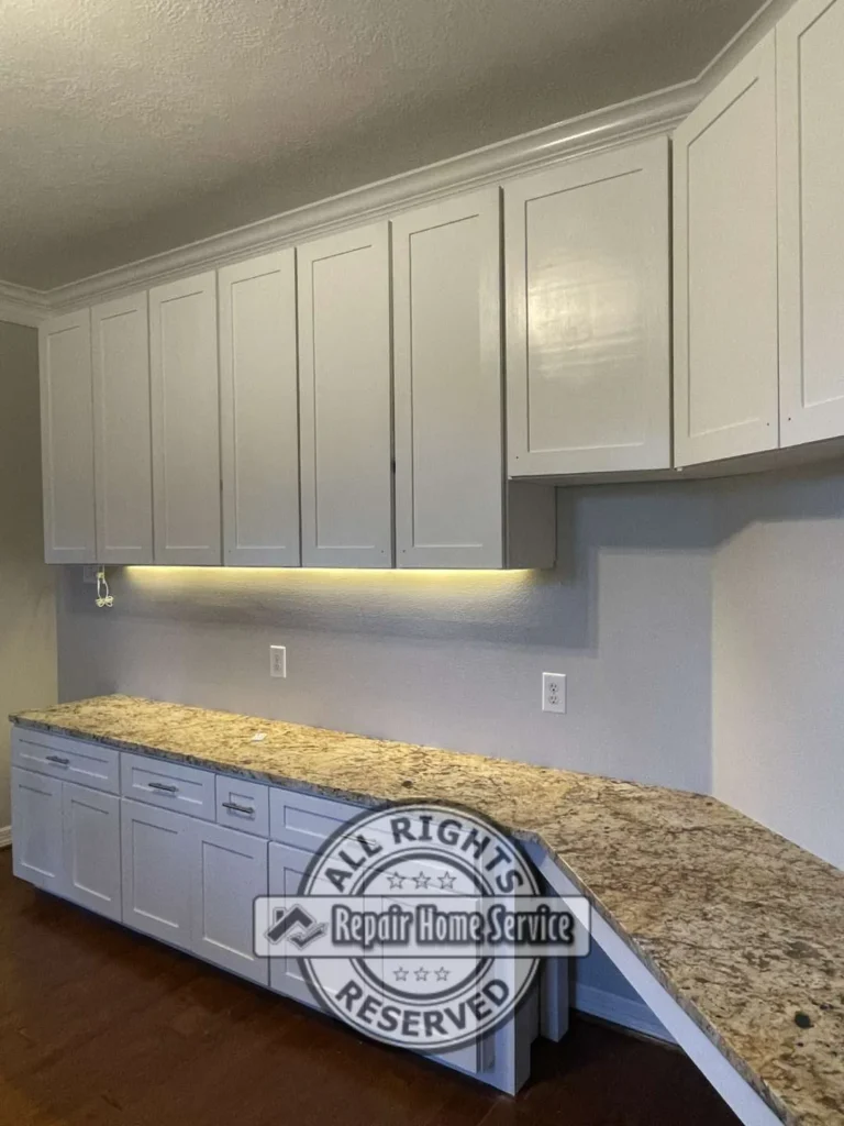 Close-up of finished white gloss shaker cabinets and speckled granite countertop in Cypress TX craft room with warm under-cabinet LED lighting and brushed metal drawer pulls.