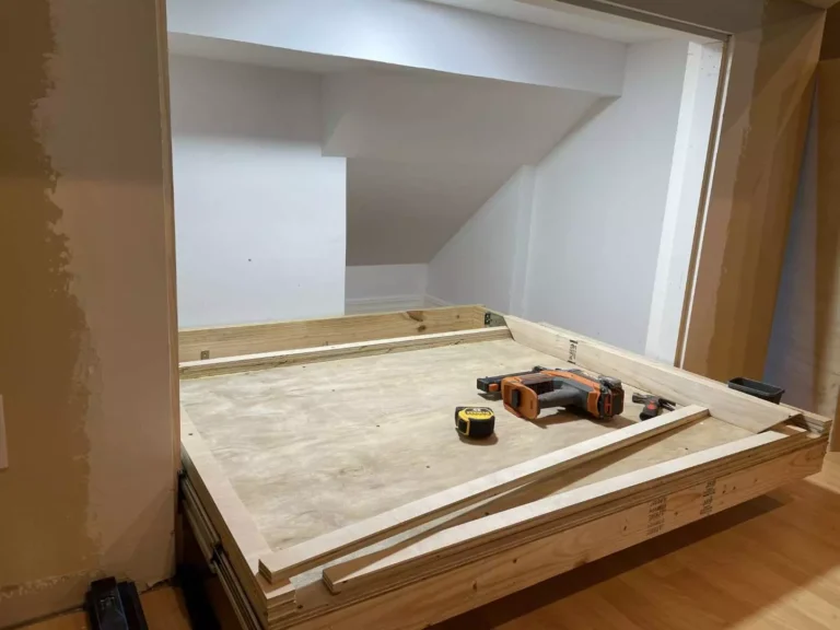 Custom blond plywood pull-out storage platform extended from under-stair wall in Houston TX with heavy-duty metal slides, poplar framing, and carpentry tools on top.