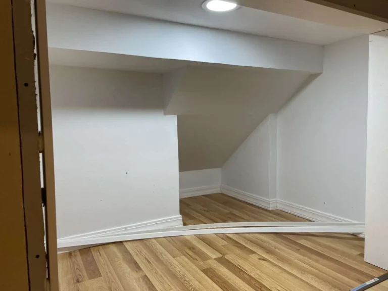 Empty under-stair storage nook in Houston TX with flat white walls, laminate wood floor, recessed LED ceiling light, and white baseboard trim before final door install.