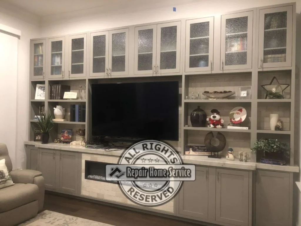 Finished custom entertainment bookcase in Houston TX with painted shaker cabinets, open shelving, glass-front upper doors, TV opening, and built-in storage