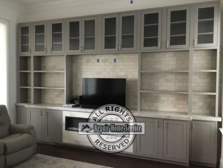 Partially completed built-in entertainment wall in Houston TX with painted lower cabinets, open shelves, glass cabinet doors, and centered TV space