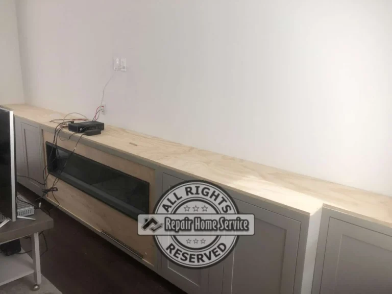 In-progress entertainment console with painted shaker cabinet doors, granite countertop, and framed opening for electric fireplace
