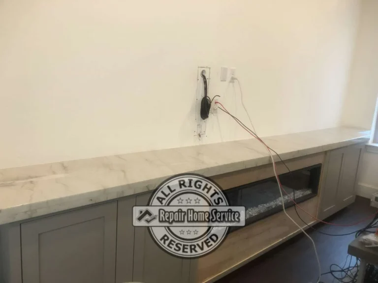 Custom entertainment console with granite counter, painted shaker cabinets, wall wiring, and fireplace opening during installation
