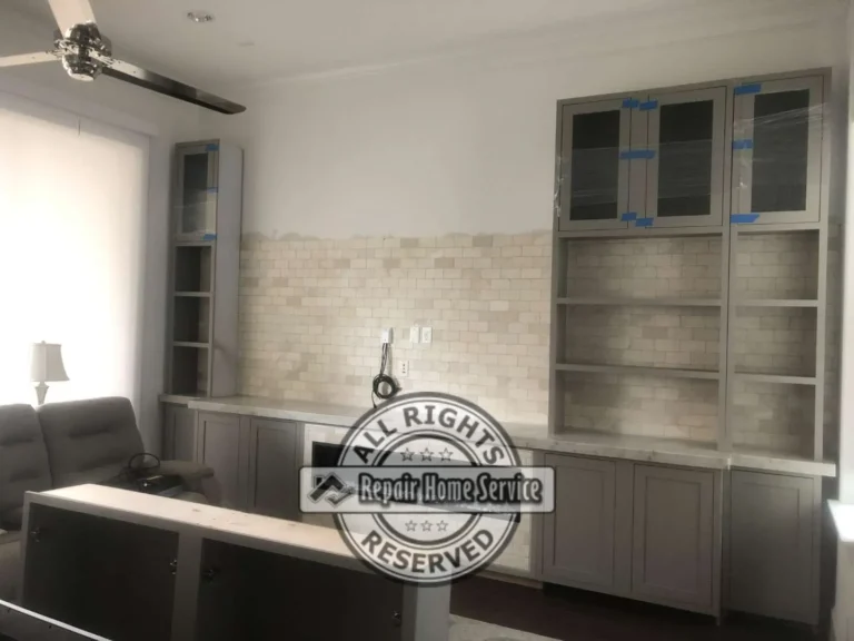 In-progress built-in bookcase with painted lower cabinets, tall side shelving, glass-front upper cabinets, and stone backsplash
