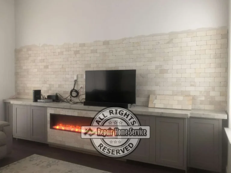 Finished electric fireplace console with natural stone surround, granite countertop, and painted shaker cabinets in Houston TX living room