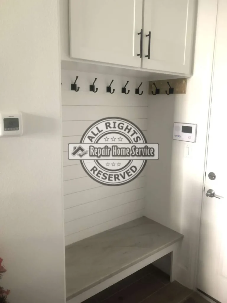 Finished mud room built-in in Houston TX with painted shaker upper cabinets, black pulls, coat hooks, shiplap-style backing, oak bench countertop, and entry door storage area.