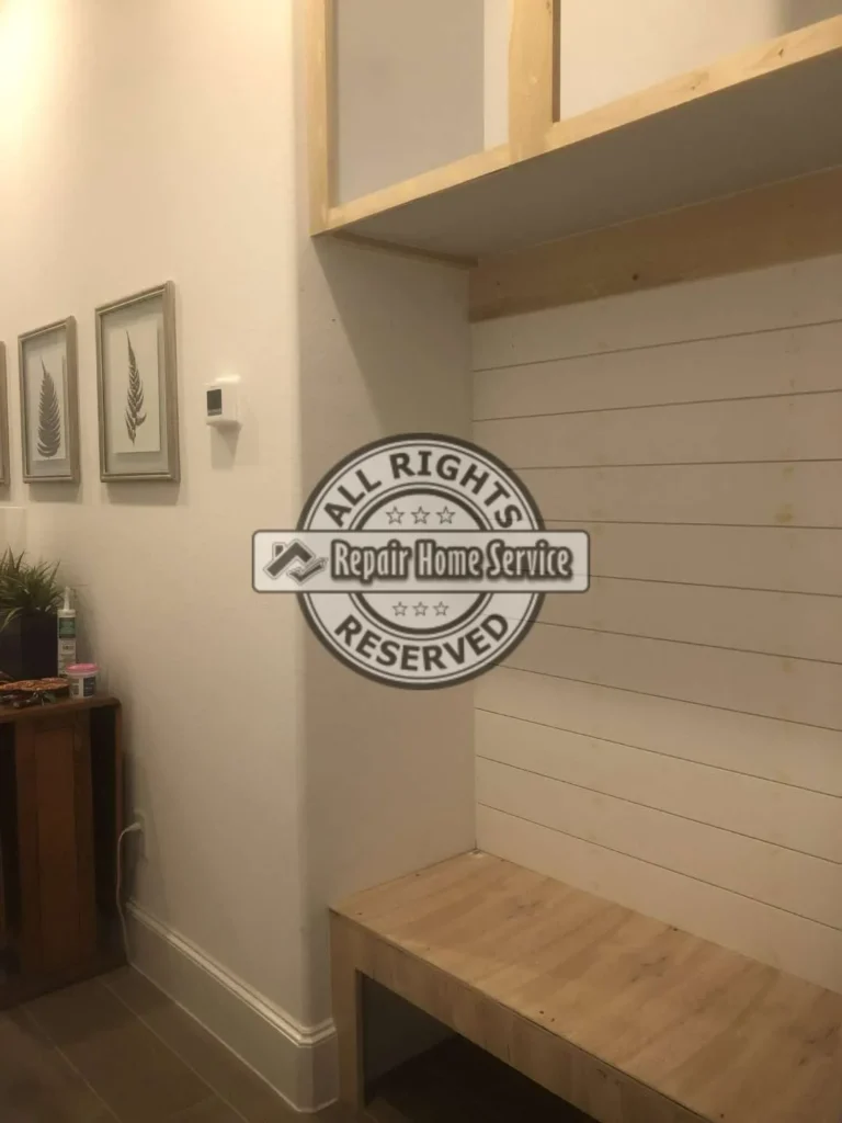 Custom mud room built-in under construction with raw wood cabinet framing, shiplap-style back panel, oak bench countertop, wall trim, and tile floor.