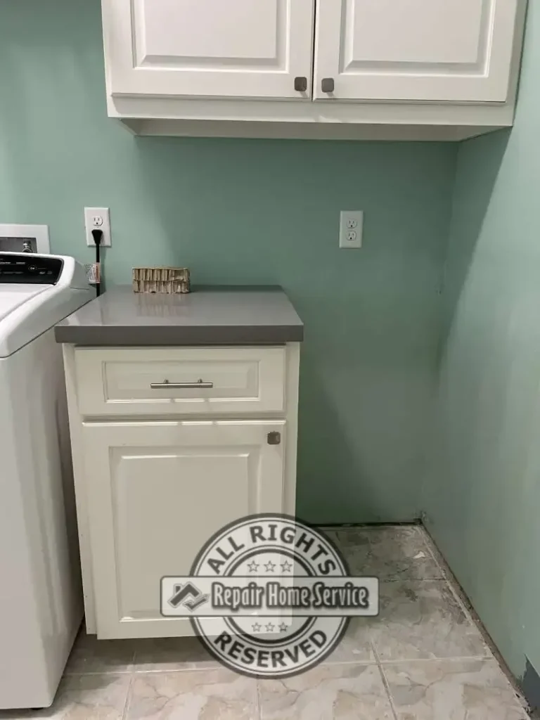 Completed laundry room cabinet renovation featuring custom drawer, white raised-panel cabinetry, gray countertop, and dedicated freezer space.