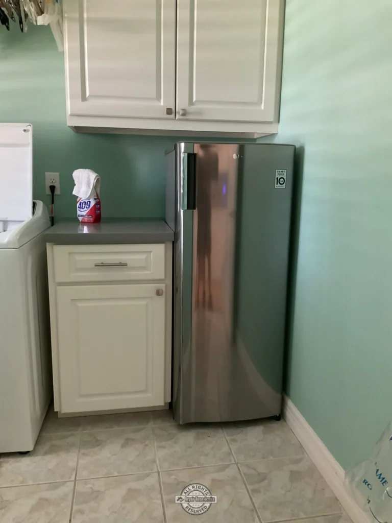 Finished laundry room storage solution with custom cabinet modifications, compact upright freezer installation, upper wall cabinets, and matching trim details in Spring TX.