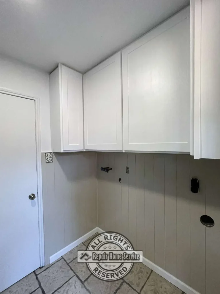 Newly installed white upper laundry room cabinets with shaker doors and clean built-in appearance.