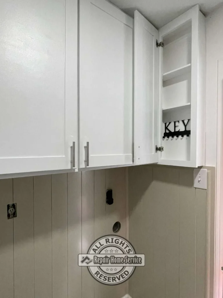 Custom white laundry room cabinetry featuring open shelving compartment and decorative key holder storage.
