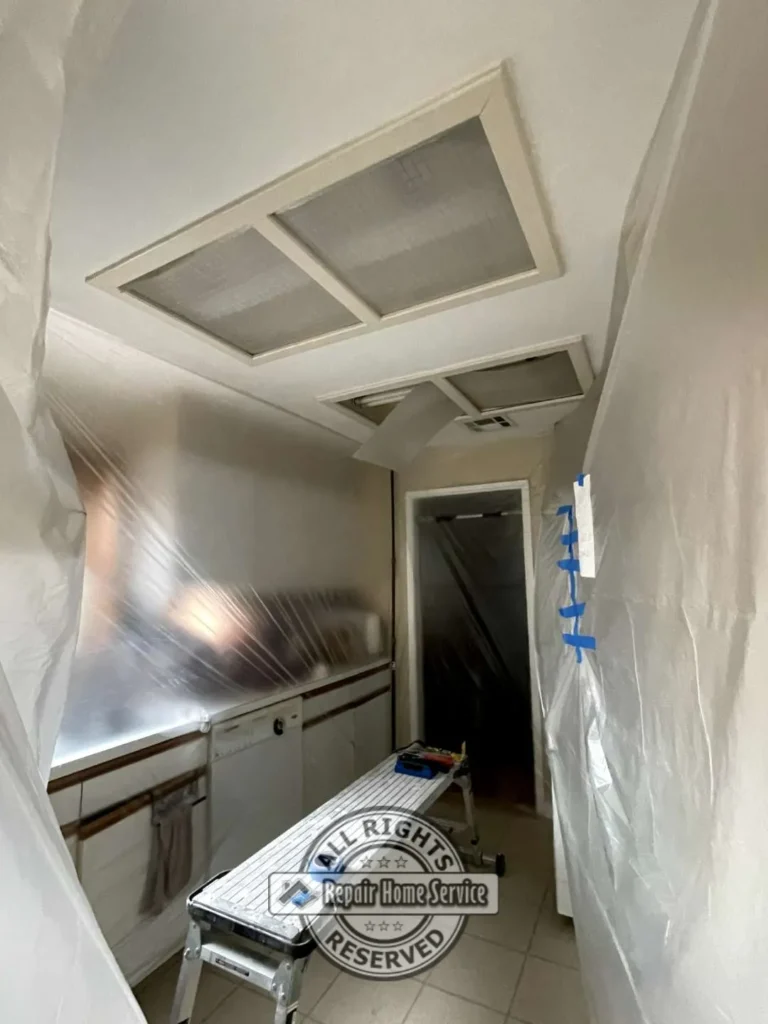 Narrow kitchen hallway with restored drywall ceiling panels, recessed lighting covers, protective plastic containment, and preparation for final ceiling finishing in Houston TX home.