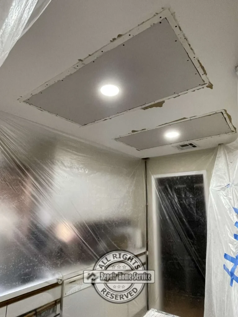 Ceiling repair preparation with recessed lighting cutouts and plastic containment protecting walls and cabinetry in Houston TX kitchen area.