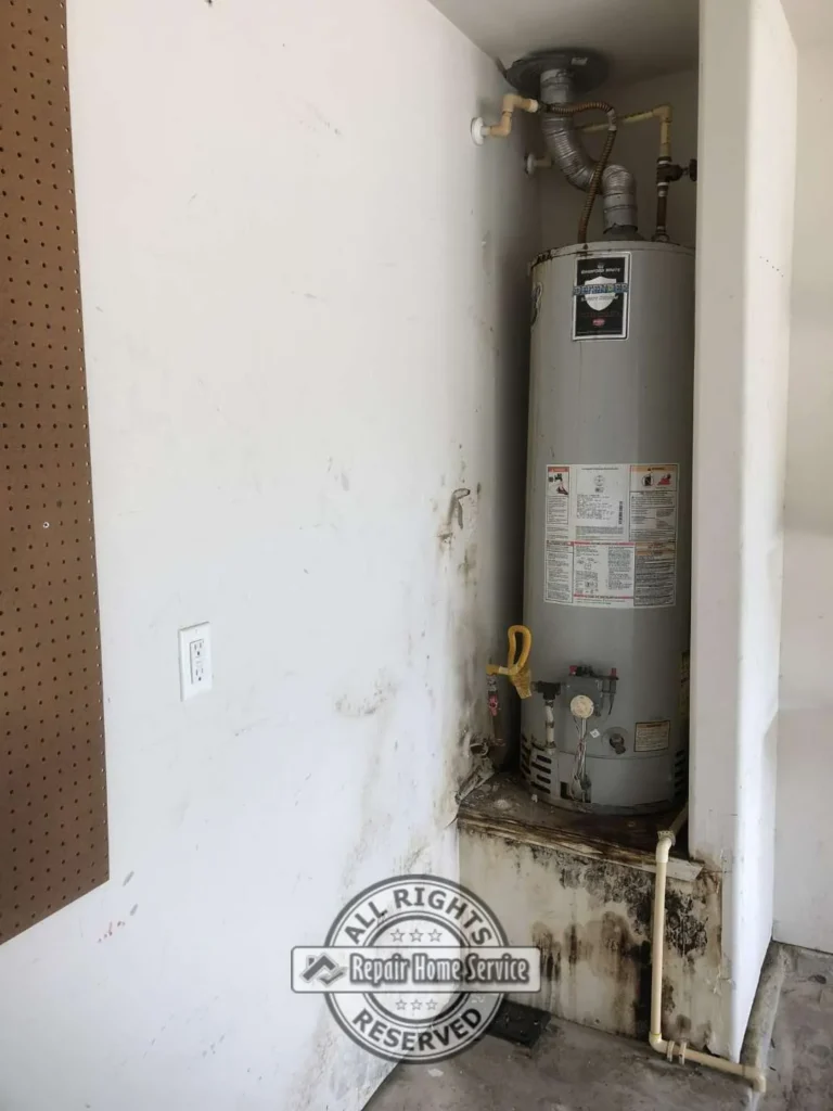 Utility closet before drywall repair showing water heater, stained wall, damaged lower drywall, pegboard, plumbing pipes, and water damage around the base.