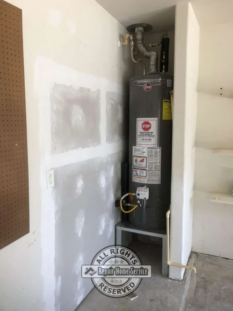 Water heater closet after Sheetrock repair with patched drywall wall, joint compound finish, plumbing pipes, built-in shelving, and utility area ready for paint.