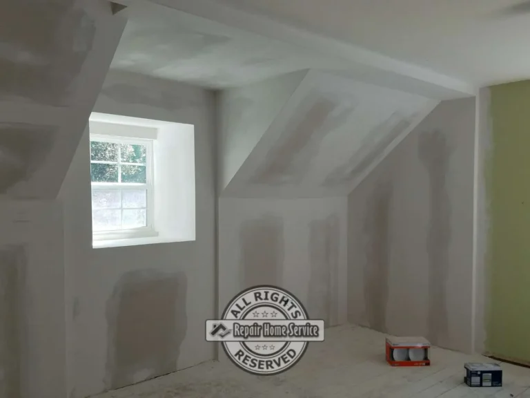 Attic-style room with repaired drywall on sloped walls and ceiling, joint compound patches, window opening, and white plank flooring.