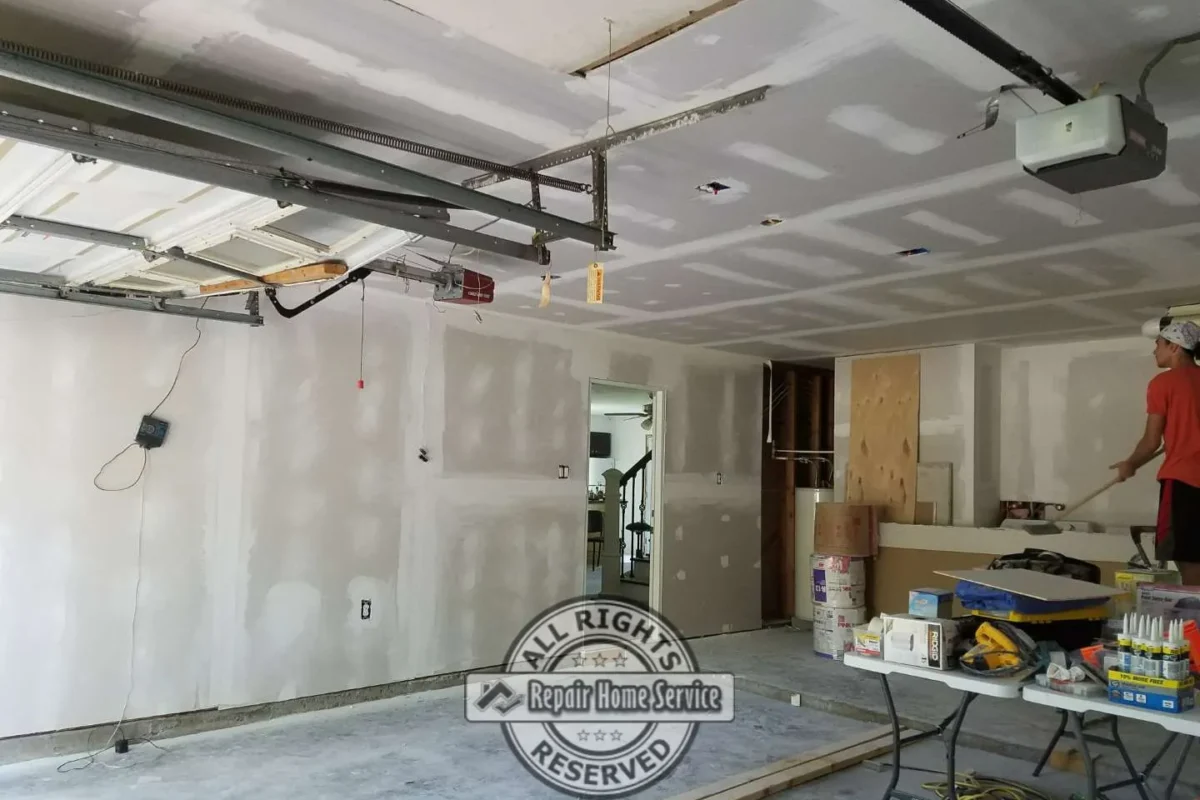 Garage Sheetrock installation in Houston TX with taped ceiling seams, patched walls, open garage door track, ceiling opener, and drywall panels ready for final finishing.