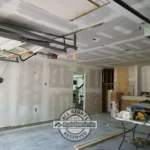 Garage Sheetrock installation in Houston TX with taped ceiling seams, patched walls, open garage door track, ceiling opener, and drywall panels ready for final finishing.