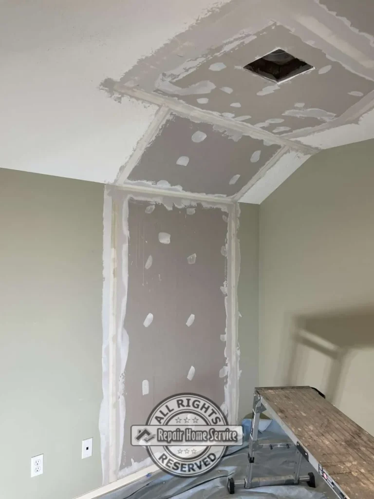 New drywall repair on bedroom wall and angled ceiling with taped seams, joint compound, vent opening, base trim, and work platform.